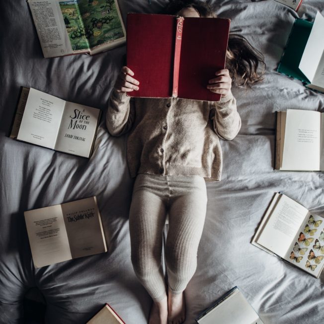 woman laying on a bed with books