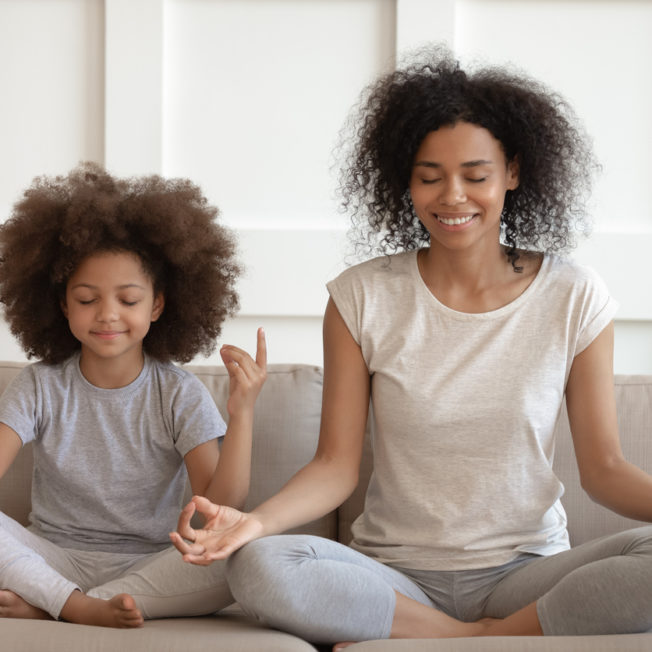 Healthy african mother teaching meditation sit with daughter on sofa